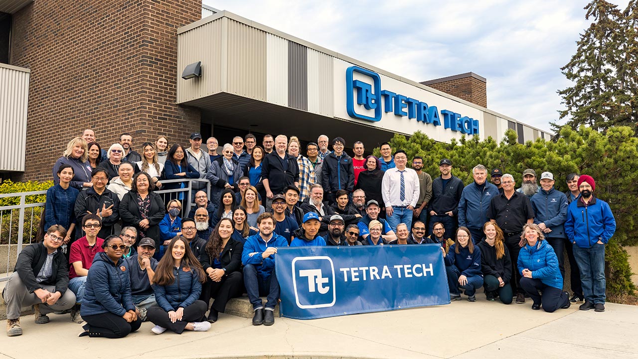 Grand groupe d'employés de Tetra Tech devant un immeuble à bureaux portant une affiche Tetra Tech