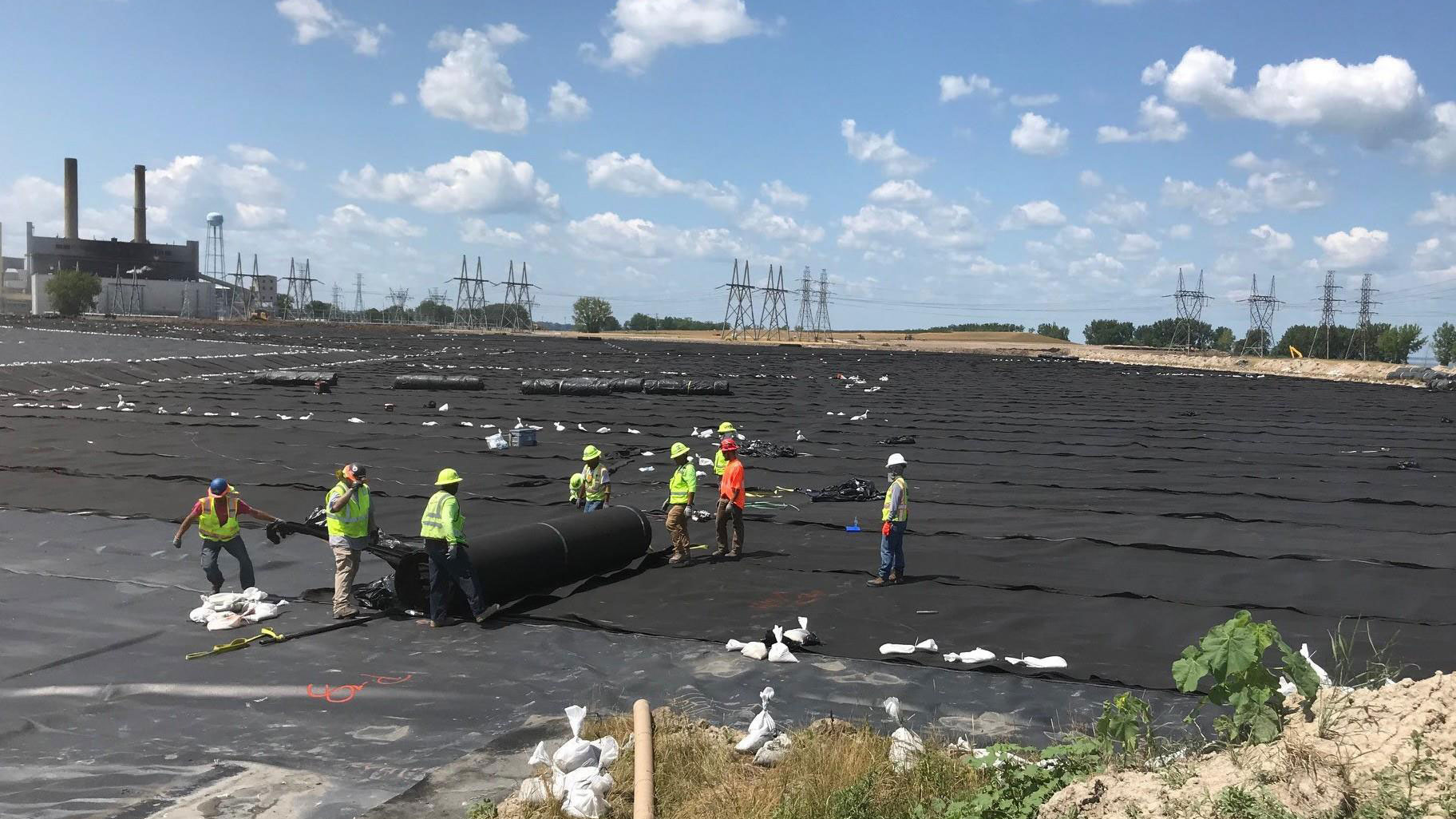 Une équipe responsable de l’étanchéité installe un géotextile sur une géomembrane précédemment installée sur une grande obturation de cendres de charbon dans une centrale électrique