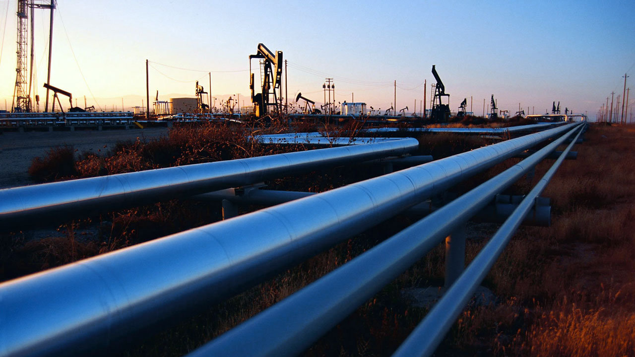 Pipelines métalliques bleus traversant un champ pétrolifère au coucher du soleil