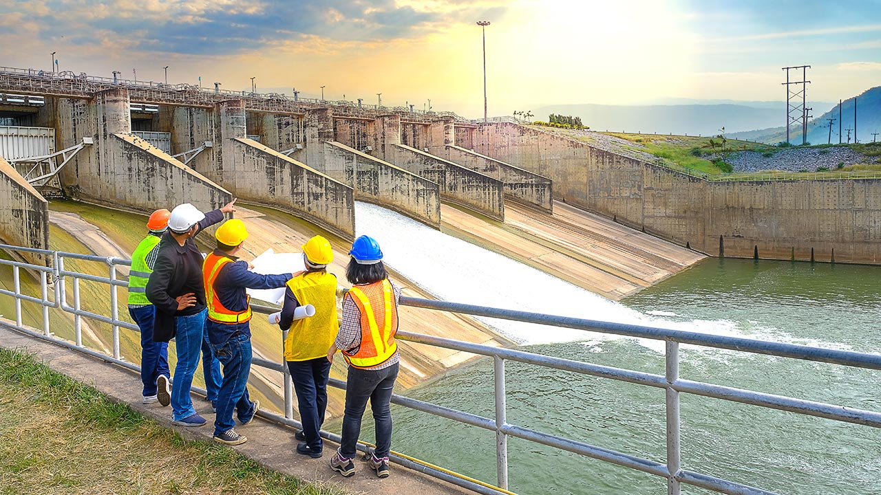 Des ingénieurs portant un EPI examinent des plans à une installation hydroélectrique
