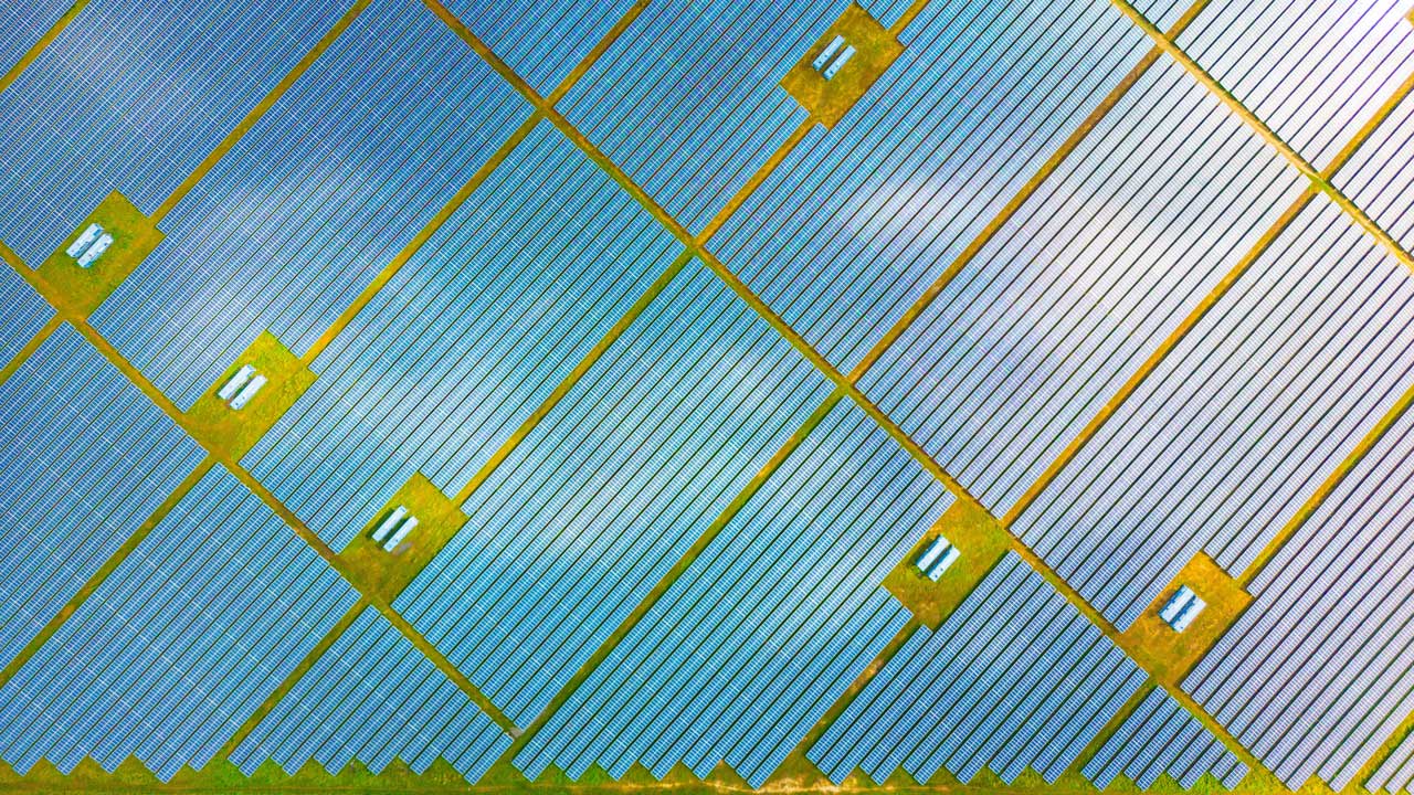 Cliché de photothèque montrant un parc solaire vu de dessus ; les champs alignés en diagonale représentent des panneaux solaires bleus sur une pelouse verte