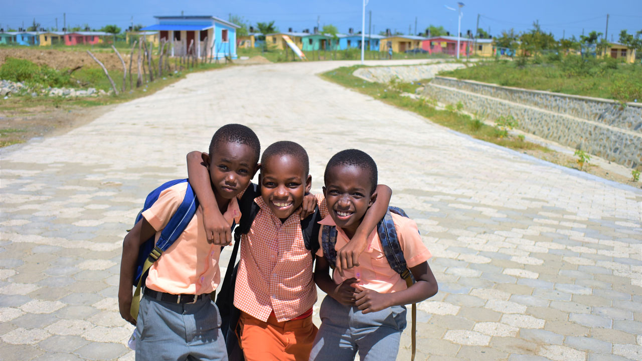 Trois jeunes garçons se tiennent devant un projet de développement de nouveaux logements à Haïti