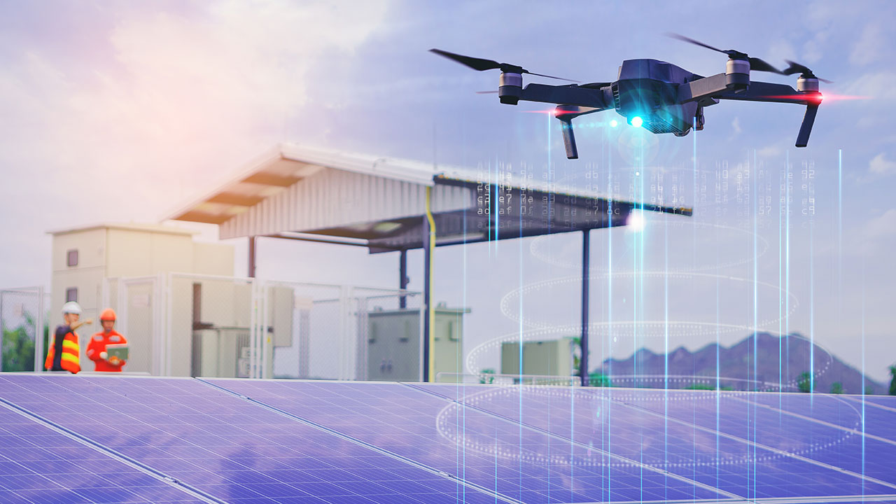 Un drone effectue un vol stationnaire au-dessus de panneaux solaires avec des ingénieurs portant un EPI en arrière-plan