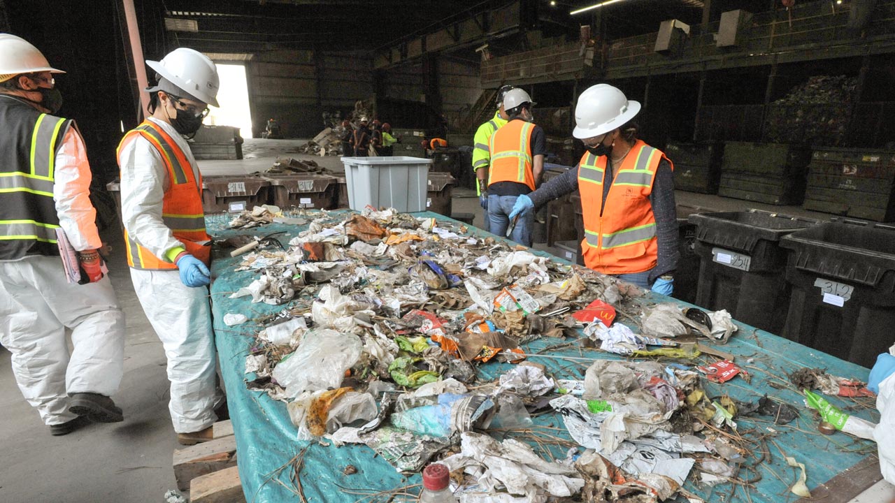Des employés portant un EPI prélèvent des échantillons de déchets résidentiels pour caractériser des pratiques d’élimination