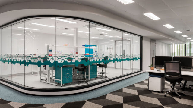 Petit espace de laboratoire à un plancher de bureaux. L’espace de laboratoire est séparé par une paroi en verre incurvée