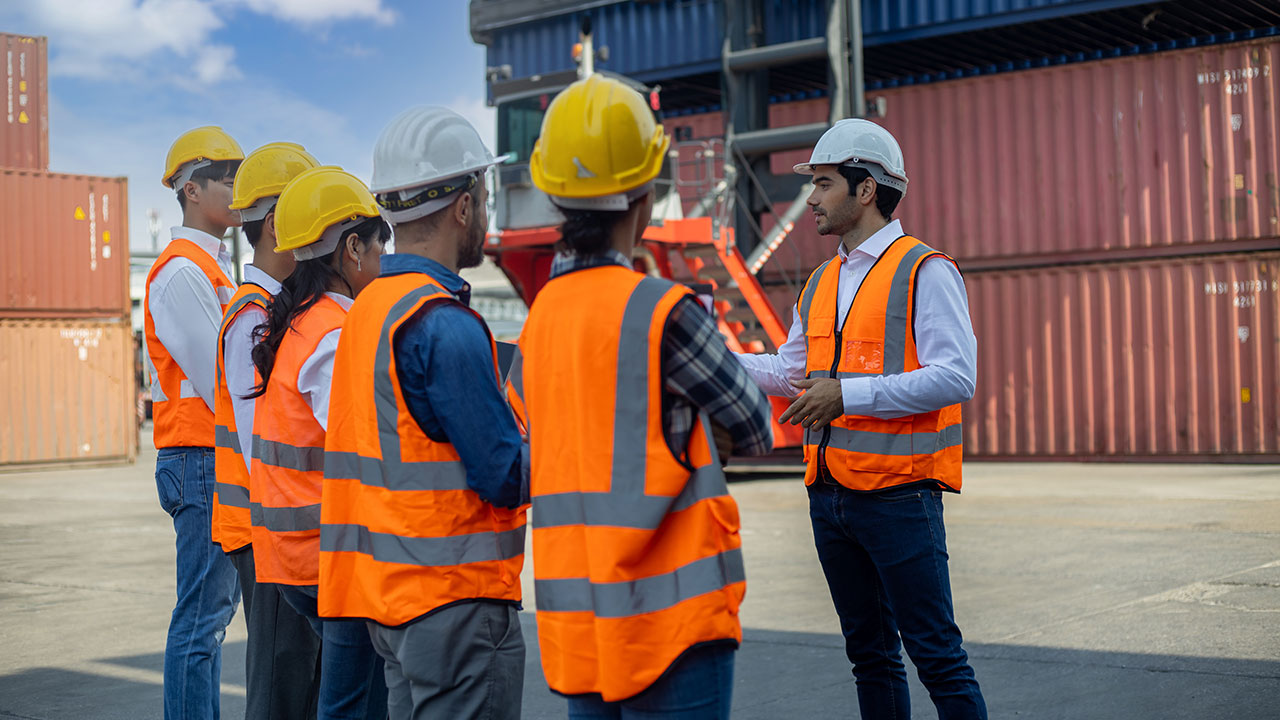 Six personnes portant des gilets de sécurité orange et un casque de sécurité se sont rassemblées pour organiser une réunion informelle sur un site de projet