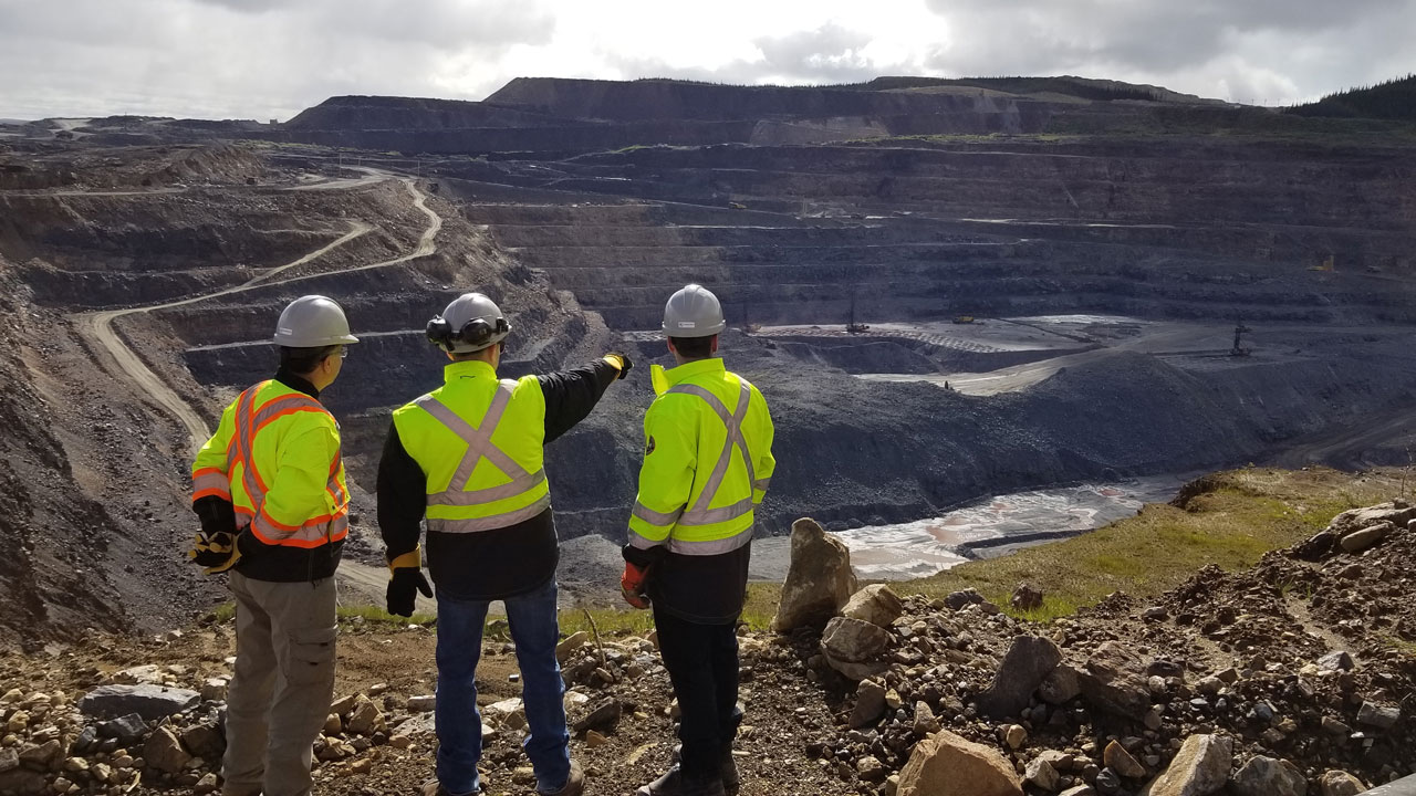 Trois techniciens en EPI observent une mine en contrebas