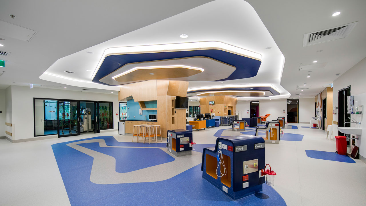 Zone de traitement hospitalier avec, sur le plancher, des concepts géométriques bleus et blancs qui sont reproduits sur le plafond et le dispositif d’éclairage