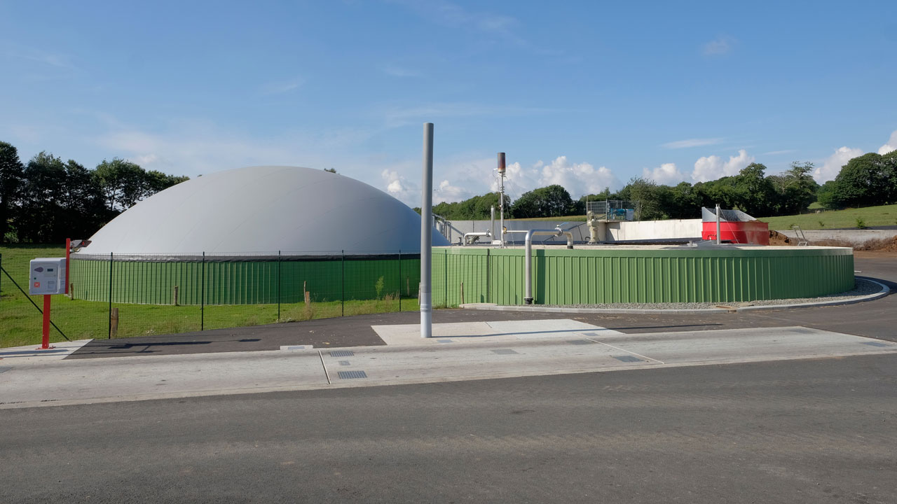 Installation de digestion anaérobie pour la transformation des déchets organiques, entourée d’une clôture et avec un ciel bleu en arrière-plan