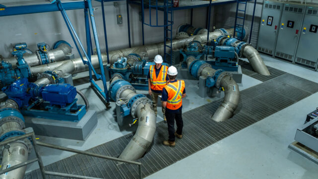 Deux ingénieurs masculins qui se trouvent dans une usine de traitement des eaux intérieures, avec plusieurs gros tuyaux